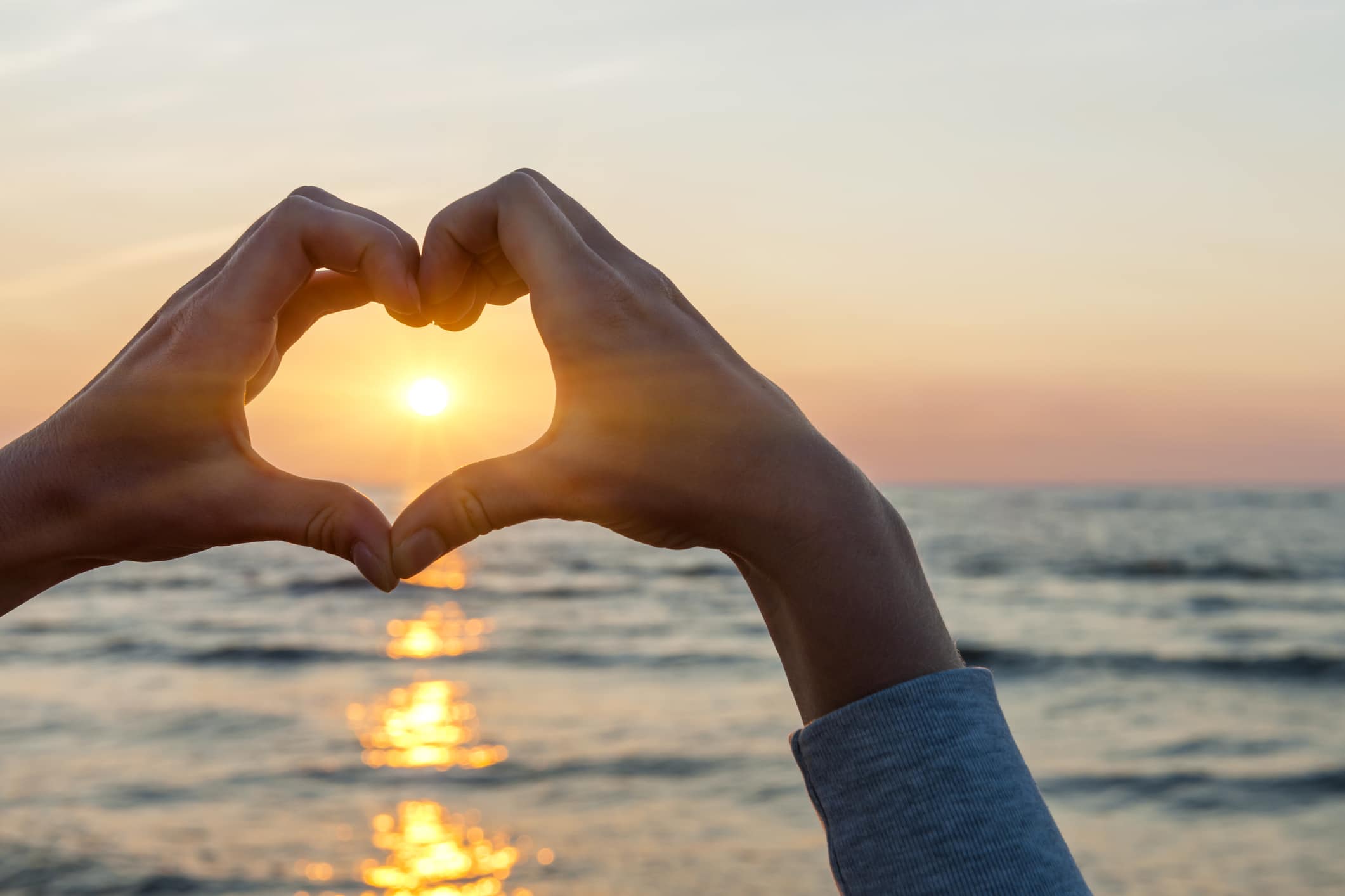 Twee handen vormen een hart om de ondergaande zon boven het water